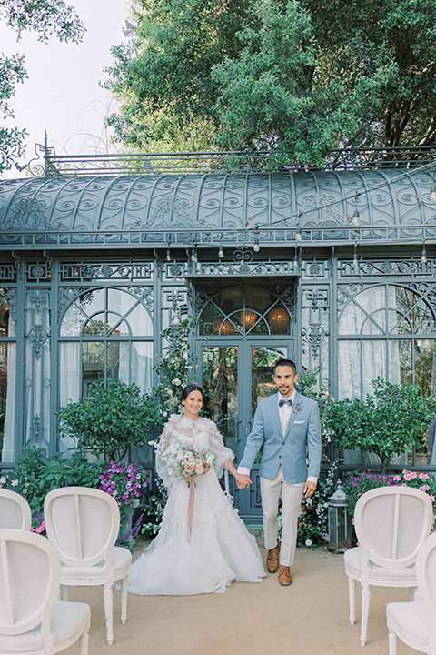  A French inspired wedding at a lavender farm with the bride in a fashion-forward white a-line gown with a high neckline and three dimensional floral appliques on it, the groom wore a light blue suit coat with a pair of tan pant and a grey velvet bow tie, couple at the ceremony