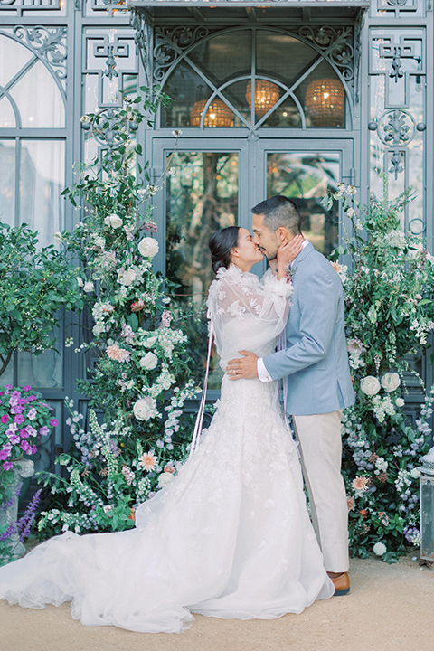  A French inspired wedding at a lavender farm with the bride in a fashion-forward white a-line gown with a high neckline and three dimensional floral appliques on it the groom wore a light blue suit coat with a pair of tan pant and a grey velvet bow tie, couple at the ceremony 