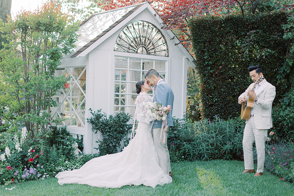 A French inspired wedding at a lavender farm with the bride in a fashion-forward white a-line gown with a high neckline and three dimensional floral appliques on it, the groom wore a light blue suit coat with a pair of tan pant and a grey velvet bow tie, they are having their first dance on the grass with musician Moses Lin Music