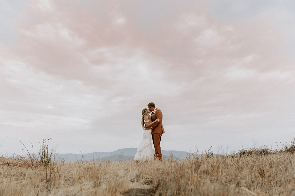  rustic boho wedding with warm colors and the bride in an off the shoulder gown and the groom in a caramel suit 