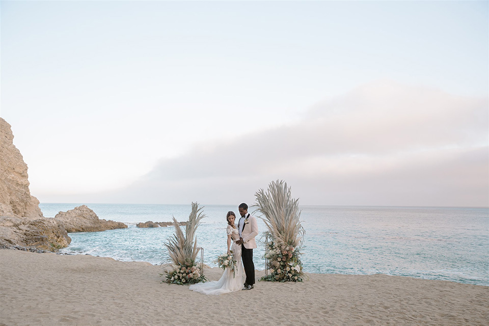  glamorous wedding at Terranea Resort in Paso Robles with the bride in a fitted lace gown with long sleeves and the groom in a blush pink tuxedo 