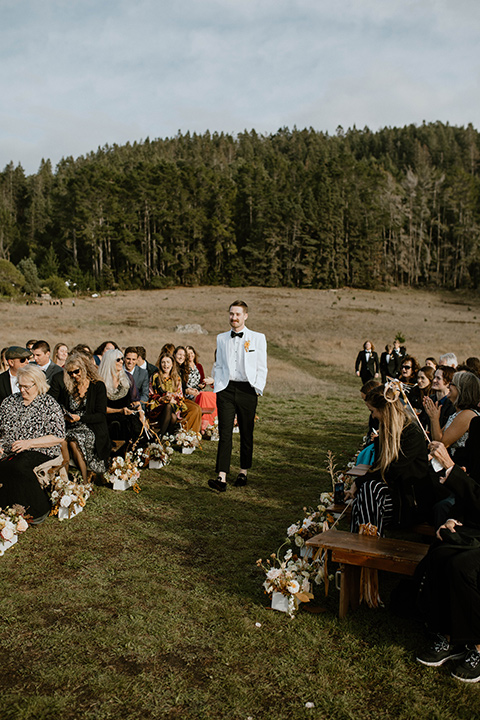  lizzie and tommys wedding on the beach with neutral colors and a gold velvet jacket – groom walking down the aisle 