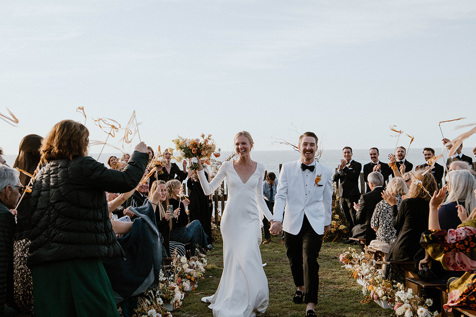  lizzie and tommys wedding on the beach with neutral colors and a gold velvet jacket – walking down the aisle