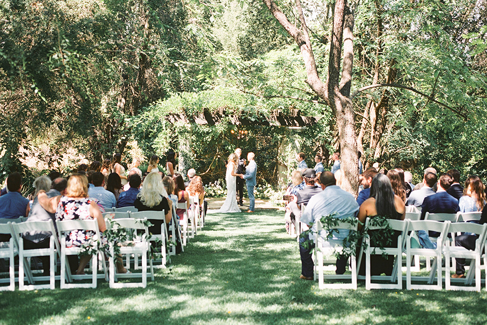  couple at their wedding ceremony with the groom in a  light blue suit and the bride in a lace long gown