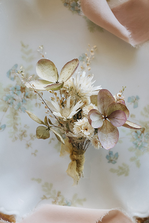  an elevated cottagecore wedding design in a barn venue with gold and tan tones – the bride in a white gown with long sleeves and the groom in a tan suit – boutonnière 