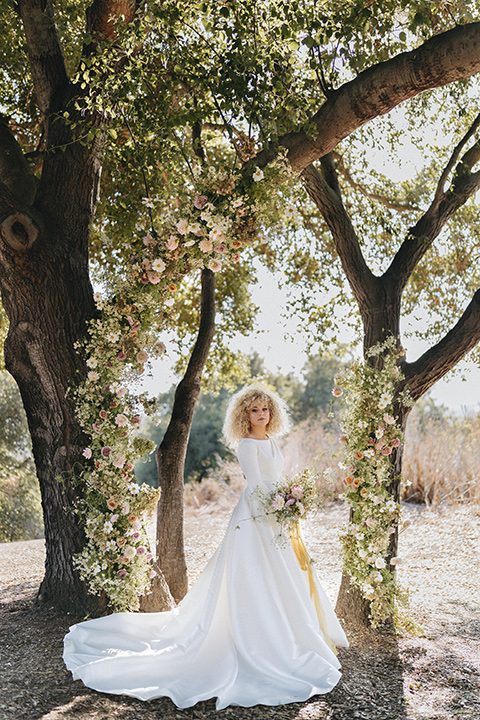  an elevated cottagecore wedding design in a barn venue with gold and tan tones – the bride in a white gown with long sleeves and the groom in a tan suit – bride 