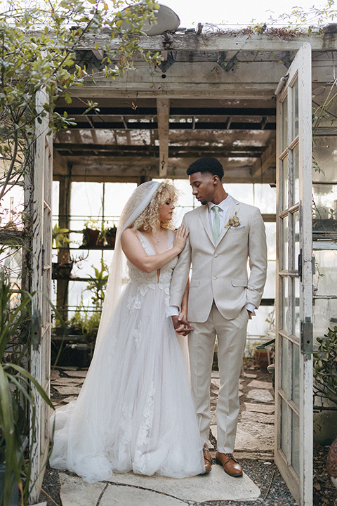  an elevated cottagecore wedding design in a barn venue with gold and tan tones – the bride in a white gown with long sleeves and the groom in a tan suit – couple embracing 