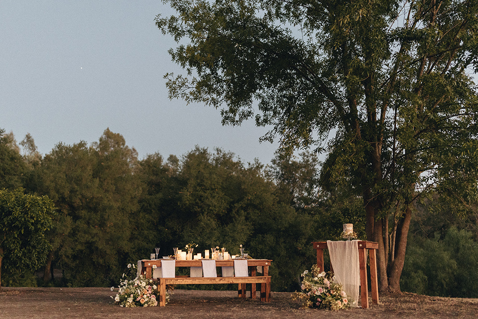  an elevated cottagecore wedding design in a barn venue with gold and tan tones – the bride in a white gown with long sleeves and the groom in a tan suit – tables 