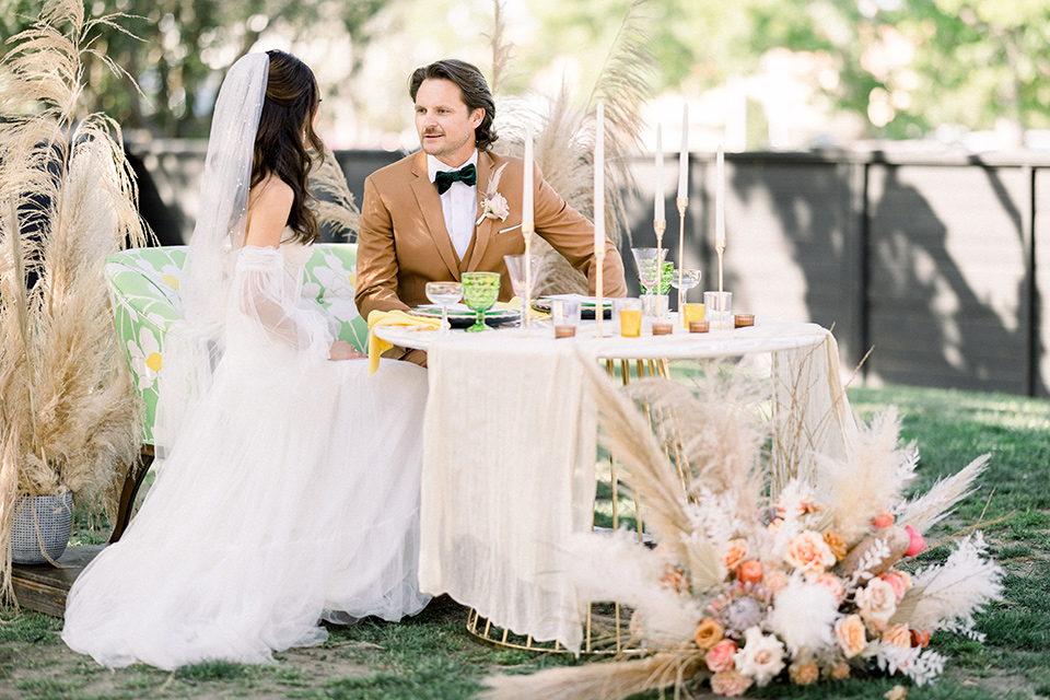  70s inspired wedding with orange and caramel tones with the bride in a lace gown and the groom in a caramel suit - couple sitting at the table 