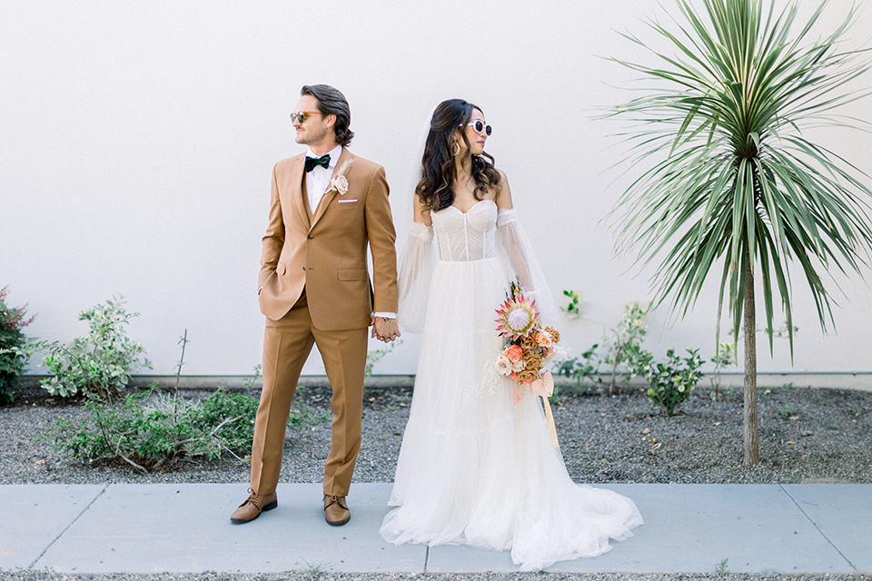  70s inspired wedding with orange and caramel tones with the bride in a lace gown and the groom in a caramel suit - couple holding hands 
