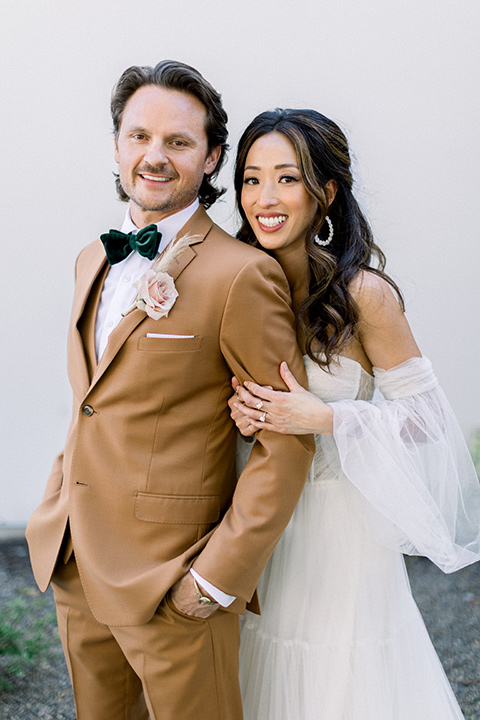  70s inspired wedding with orange and caramel tones with the bride in a lace gown and the groom in a caramel suit - couple smiling outside 