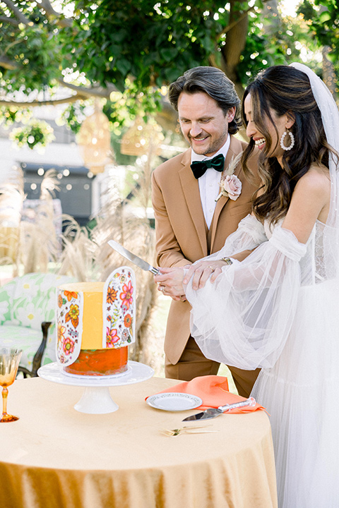  70s inspired wedding with orange and caramel tones with the bride in a lace gown and the groom in a caramel suit - cutting the cake 