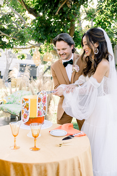  70s inspired wedding with orange and caramel tones with the bride in a lace gown and the groom in a caramel suit - cutting the cake 