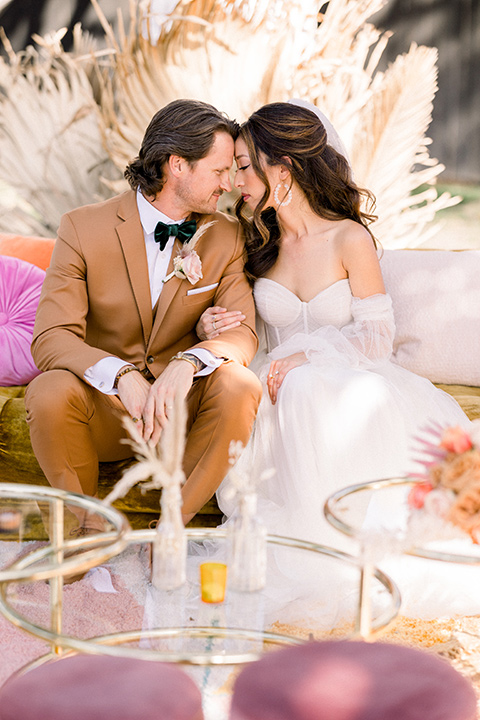  70s inspired wedding with orange and caramel tones with the bride in a lace gown and the groom in a caramel suit - sitting at the table 