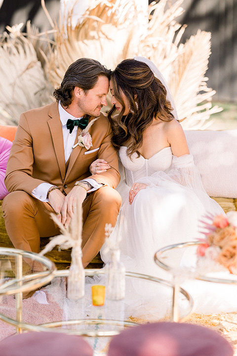  70s inspired wedding with orange and caramel tones with the bride in a lace gown and the groom in a caramel suit - sitting at the table 