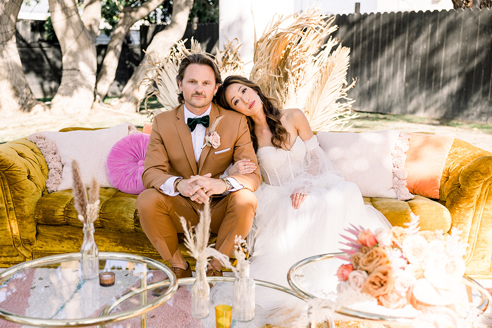  70s inspired wedding with orange and caramel tones with the bride in a lace gown and the groom in a caramel suit - sitting together 