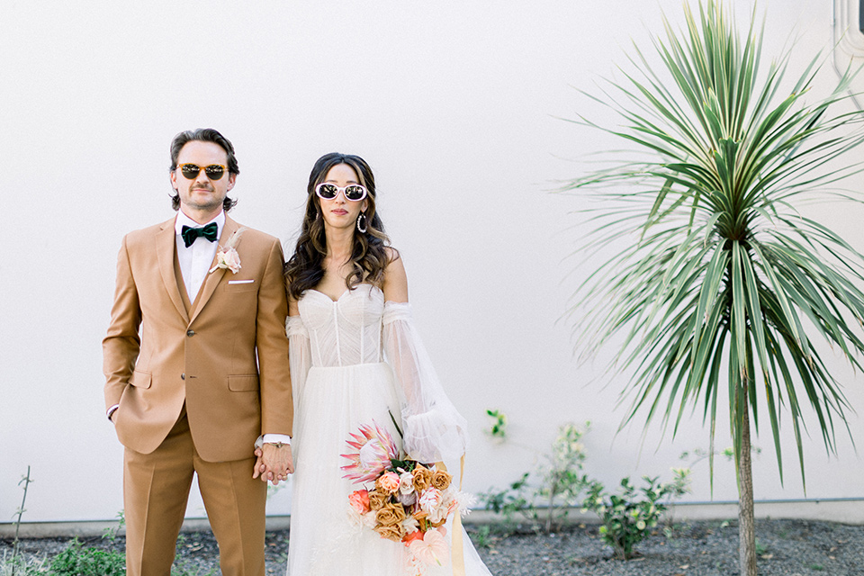 70s inspired wedding with orange and caramel tones with the bride in a lace gown and the groom in a caramel suit - outside 