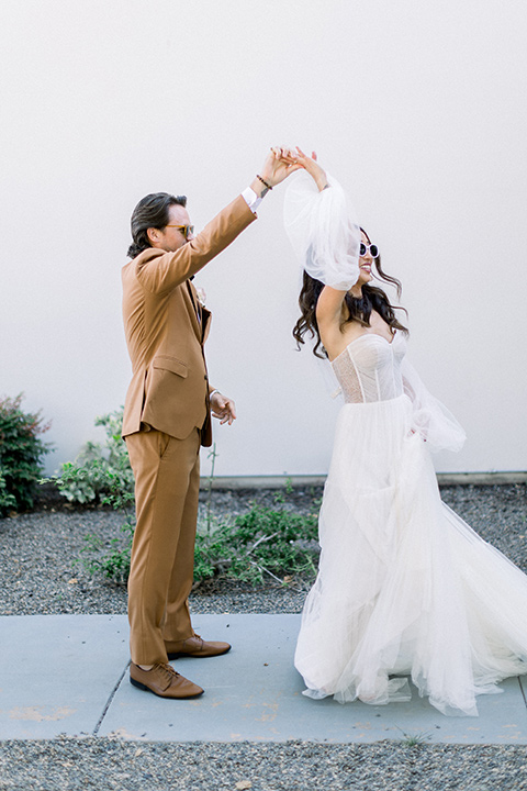  70s inspired wedding with orange and caramel tones with the bride in a lace gown and the groom in a caramel suit - couple smiling  and dancing outside 