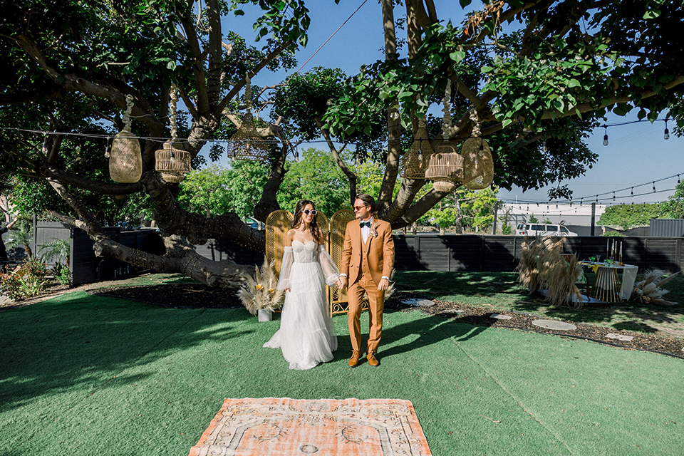  70s inspired wedding with orange and caramel tones with the bride in a lace gown and the groom in a caramel suit - walking down the aisle 