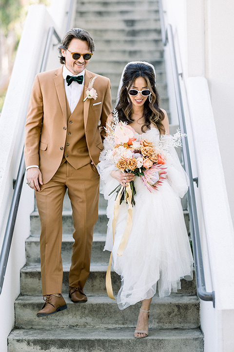 70s inspired wedding with orange and caramel tones with the bride in a lace gown and the groom in a caramel suit - walking down the stairs 
