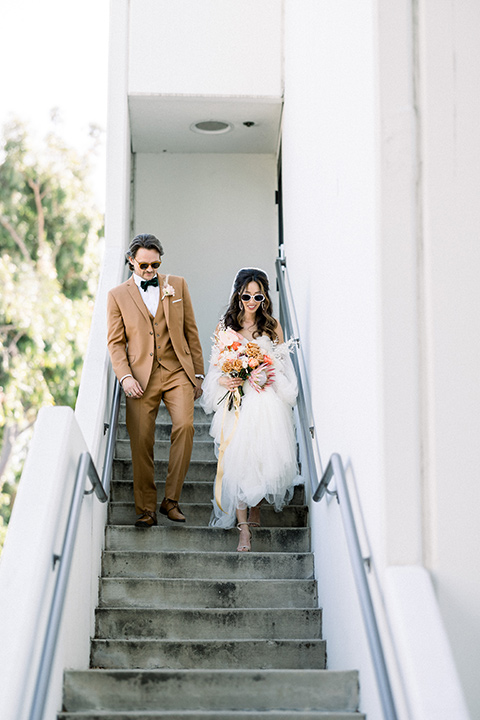 70s inspired wedding with orange and caramel tones with the bride in a lace gown and the groom in a caramel suit - walking down the stairs 