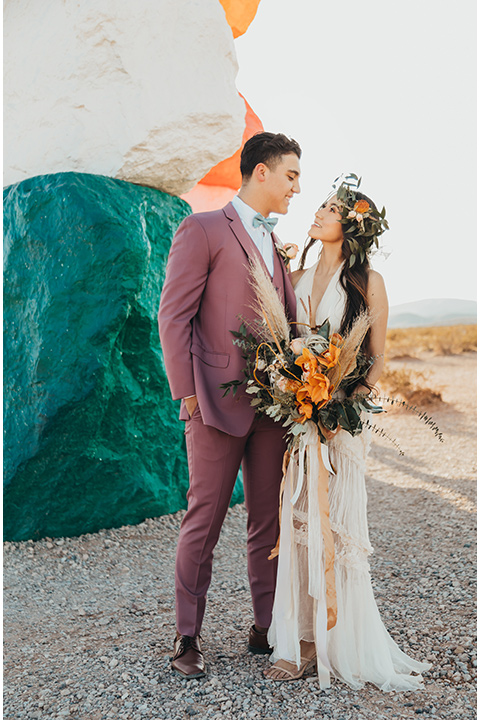  a boho elopement at the seven magical mountains in Las Vegas – the bride in a boho gown and the groom in a rose pink suit 