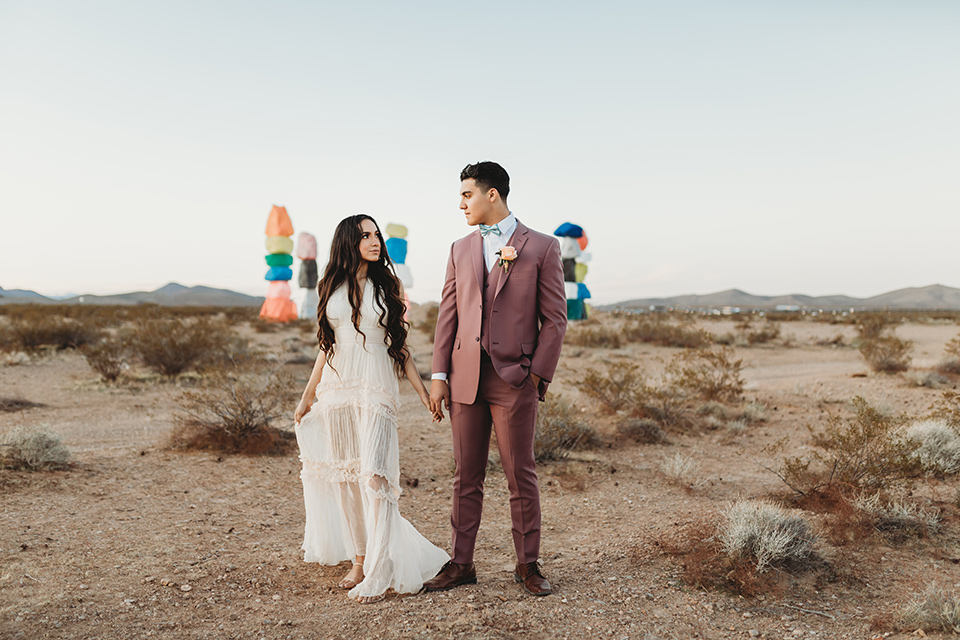  a boho elopement at the seven magical mountains in Las Vegas – the bride in a boho gown and the groom in a rose pink suit 