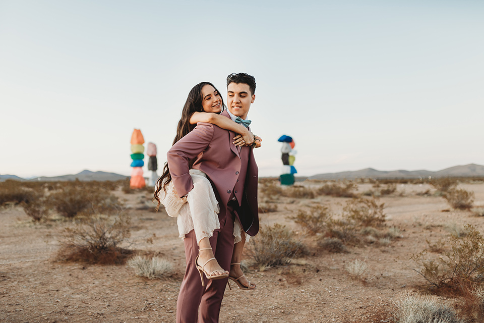  a boho elopement at the seven magical mountains in Las Vegas – the bride in a boho gown and the groom in a rose pink suit 