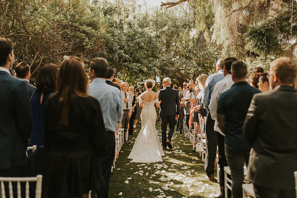  a romantic rustic garden wedding with the groom in a blue suit and floral tie and the bride in a lace gown - bride walking down the aisle 