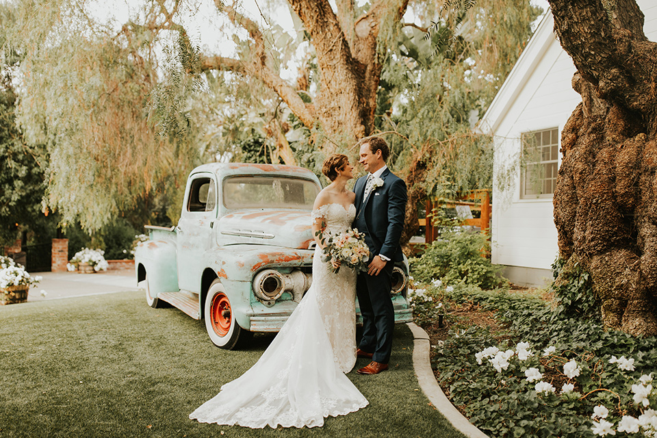  a romantic rustic garden wedding with the groom in a blue suit and floral tie and the bride in a lace gown - couple by the truck 