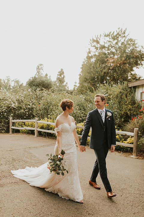  a romantic rustic garden wedding with the groom in a blue suit and floral tie and the bride in a lace gown - couple walking 