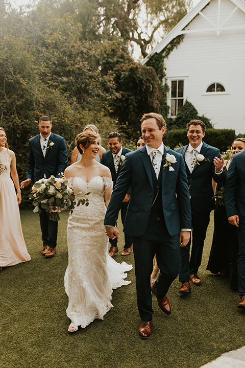  a romantic rustic garden wedding with the groom in a blue suit and floral tie and the bride in a lace gown - couple walking 