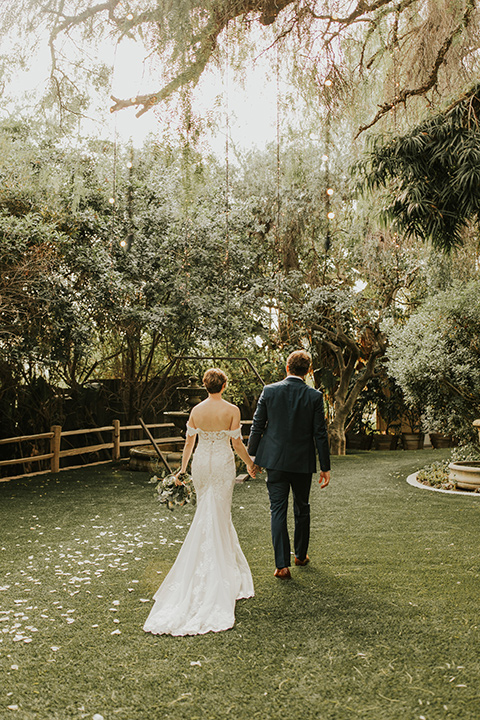  a romantic rustic garden wedding with the groom in a blue suit and floral tie and the bride in a lace gown - couple walking 