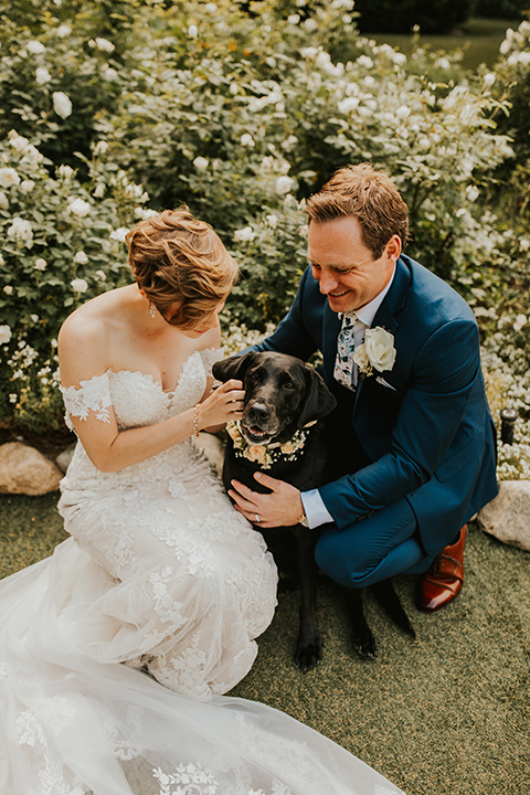  a romantic rustic garden wedding with the groom in a blue suit and floral tie and the bride in a lace gown - couple with dog 