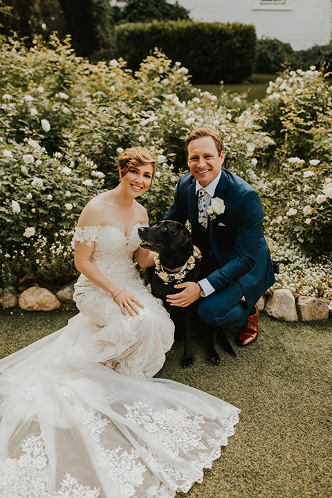  a romantic rustic garden wedding with the groom in a blue suit and floral tie and the bride in a lace gown - couple with dog 