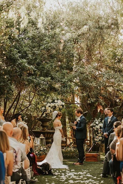  a romantic rustic garden wedding with the groom in a blue suit and floral tie and the bride in a lace gown - couple saying vows 