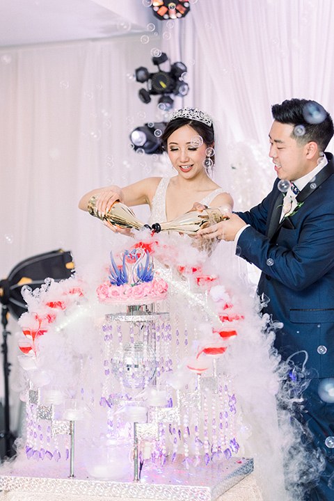  a grand cultural wedding with lion dancers and gold details – bride in a long gown with cape and groom in navy shawl tuxedo – couple pouring drinks 