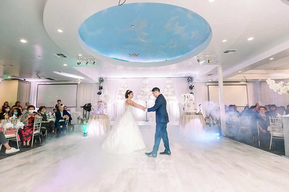  a grand cultural wedding with lion dancers and gold details – bride in a long gown with cape and groom in navy shawl tuxedo – first dance 