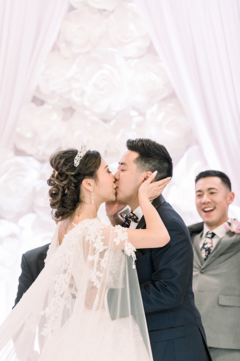  a grand cultural wedding with lion dancers and gold details – bride in a long gown with cape and groom in navy shawl tuxedo – first kiss 