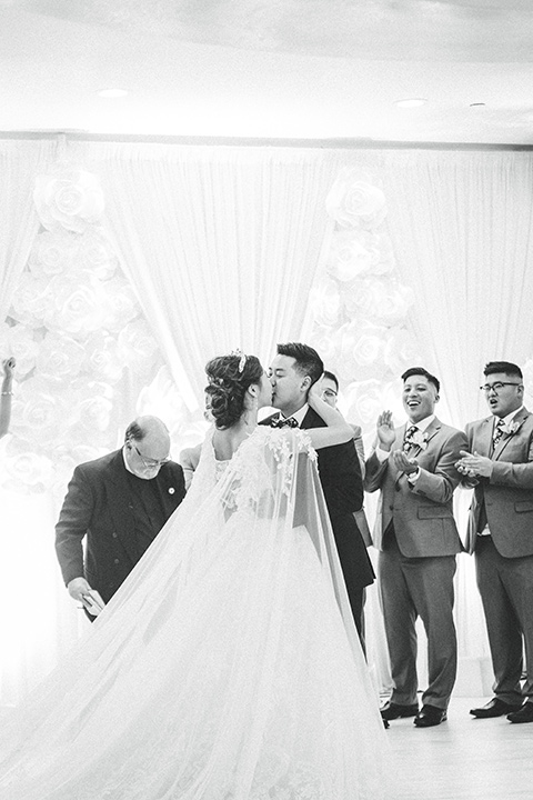  a grand cultural wedding with lion dancers and gold details – bride in a long gown with cape and groom in navy shawl tuxedo – first kiss 