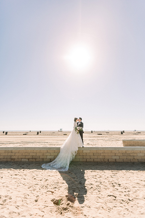  a grand cultural wedding with lion dancers and gold details – bride in a long gown with cape and groom in navy shawl tuxedo – couple by the ocean 