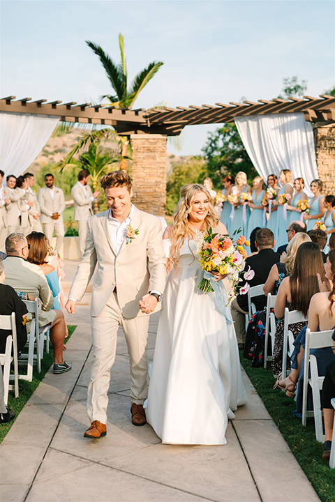  a beachy wedding with bold pastel colors and fun details - couple walking down the aisle 