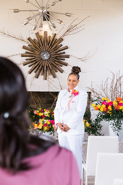 bright and bold lesbian wedding in Palm Springs with one bride in a rose pink suit and the other in a white suit – waling down the aisle