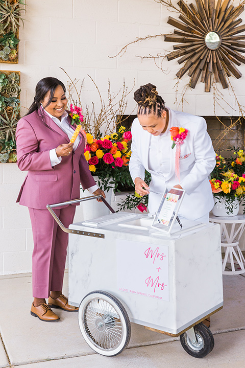  bright and bold lesbian wedding in Palm Springs with one bride in a rose pink suit and the other in a white suit – popsicle cart