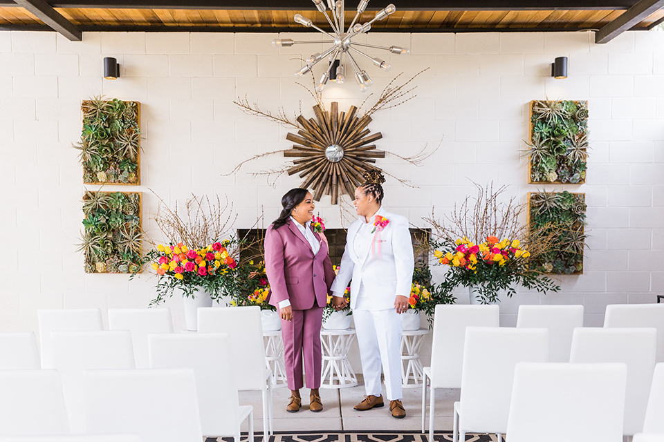  bright and bold lesbian wedding in Palm Springs with one bride in a rose pink suit and the other in a white suit – walking down the aisle