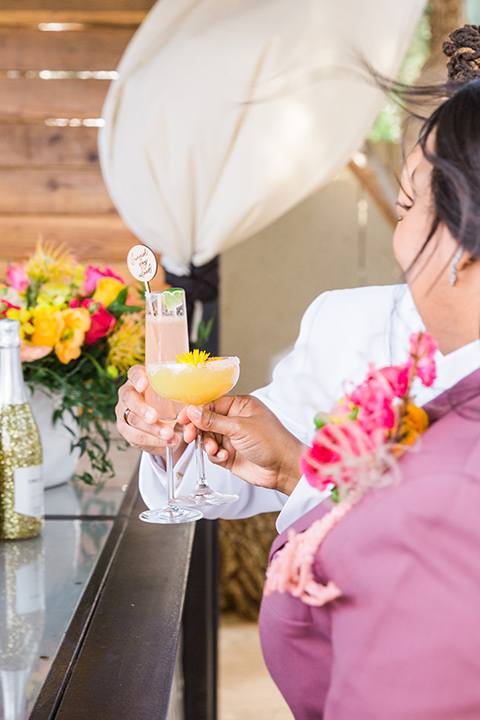  bright and bold lesbian wedding in Palm Springs with one bride in a rose pink suit and the other in a white suit – cheersing