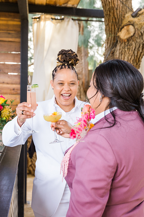  bright and bold lesbian wedding in Palm Springs with one bride in a rose pink suit and the other in a white suit – cheersing 