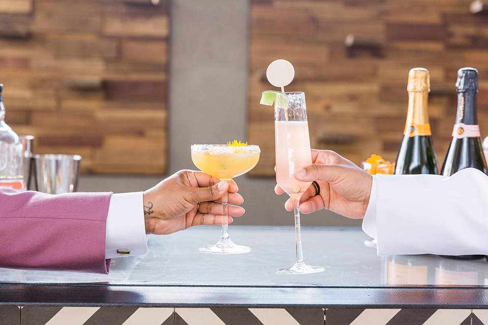  bright and bold lesbian wedding in Palm Springs with one bride in a rose pink suit and the other in a white suit – cheers