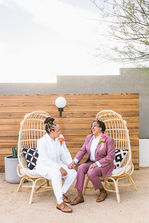  bright and bold lesbian wedding in Palm Springs with one bride in a rose pink suit and the other in a white suit – sitting at the venue