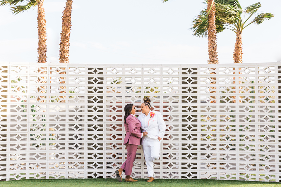  bright and bold lesbian wedding in Palm Springs with one bride in a rose pink suit and the other in a white suit – couple outside of venue